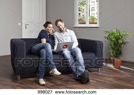 Stock Photo - A young couple using a laptop together in their living room. Fotosearch