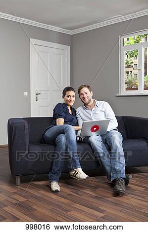 A young couple using a laptop together in their living room View Large Photo Image Stock Photograph - A young couple using a laptop together in their living room. Fotosearch
