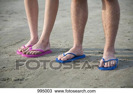 Stock Image - A young couple wearing flip-flops at the beach, low section. Fotosearch