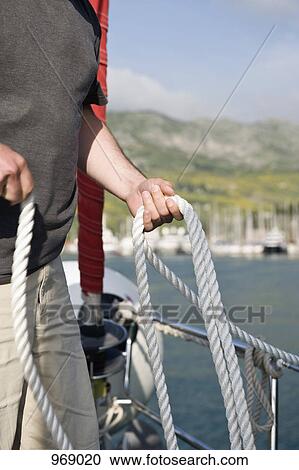 Man on a sailboat holding rope View Large Photo Image Stock Image - Man on a sailboat holding rope. Fotosearch