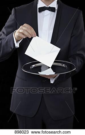 Stock Image - Midsection of a man wearing a tuxedo and holding an envelope above a silver platter. Fotosearch