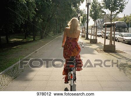 Rear view of a woman riding a bicycle on a footpath View Large Photo Image Stock Image - Rear view of a woman riding a bicycle on a footpath. Fotosearch