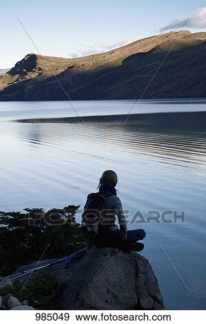 Rear view of a woman sitting by a lake, Torres del Paine National Park, Chile View Large Photo Image Stock Photo - Rear view of a woman sitting by a lake, Torres del Paine National Park, Chile. Fotosearch