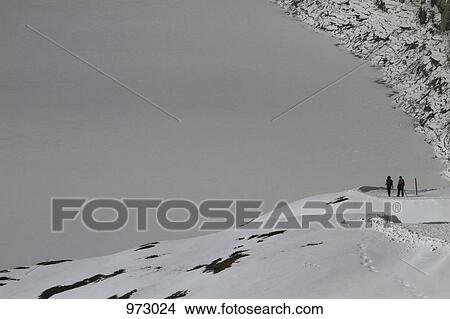 Picture - Two people walking along a snowy mountain footpath. Fotosearch