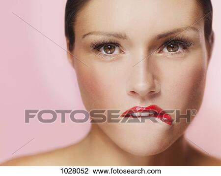 Stock Image - A beautiful woman biting her red painted lips. Fotosearch