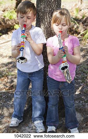 A boy and a girl standing by a tree and playing toy musical instruments View Large Photo Image Stock Image - A boy and a girl standing by a tree and playing toy musical instruments. Fotosearch