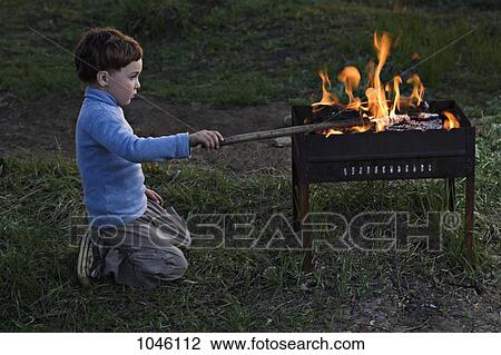 A boy poking at a fire in an outdoor fire pit View Large Photo Image Stock Image - A boy poking at a fire in an outdoor fire pit. Fotosearch