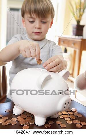 A boy putting coins into a piggy bank View Large Photo Image Stock Photo - A boy putting coins into a piggy bank. Fotosearch