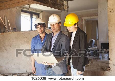 A building contractor and architects looking at a laptop at a building site View Large Photo Image Stock Photo - A building contractor and architects looking at a laptop at a building site. Fotosearch