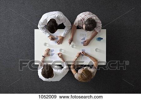 A business meeting with three businessmen and a businesswoman, overhead view View Large Photo Image Stock Photo - A business meeting with three businessmen and a businesswoman, overhead view. Fotosearch