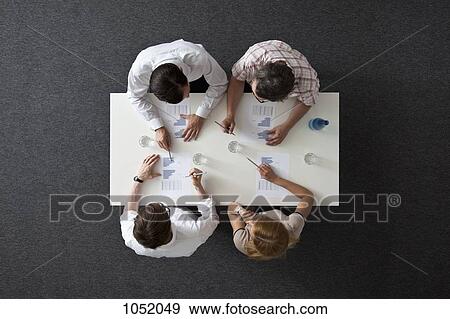 Stock Photo - A business meeting with three businessmen and a businesswoman, overhead view. Fotosearch