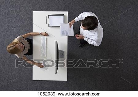 A businessman giving papers to a businesswoman sitting at a desk, overhead view View Large Photo Image Stock Photo - A businessman giving papers to a businesswoman sitting at a desk, overhead view. Fotosearch
