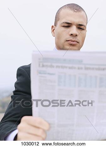 Stock Image - A businessman on a break reading a newspaper outdoors. Fotosearch