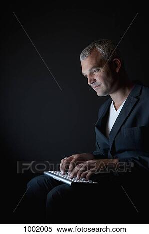 A businessman typing on a computer keyboard in the dark View Large Photo Image Stock Photography - A businessman typing on a computer keyboard in the dark. Fotosearch