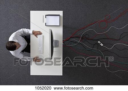 Stock Image - A businessman working at a desk with multiple cables running under it, overhead view. Fotosearch