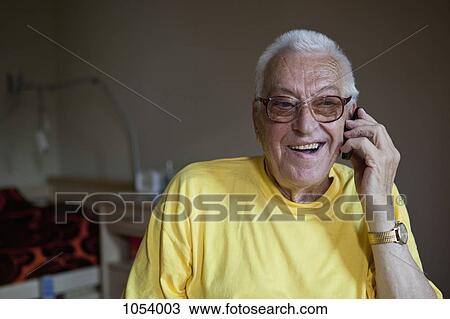 Stock Image - A cheerful senior man living in a nursing home, using a mobile phone. Fotosearch