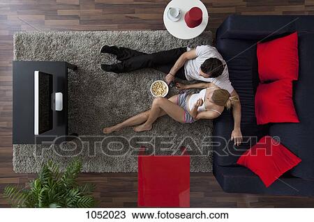 Stock Image - A couple eating popcorn and watching TV in their living room, overhead view. Fotosearch