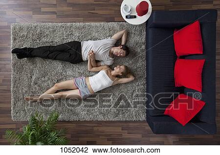 A couple lying on a living room rug, holding hands and gazing at each other, overhead view View Large Photo Image Stock Image - A couple lying on a living room rug, holding hands and gazing at each other, overhead view. Fotosearch