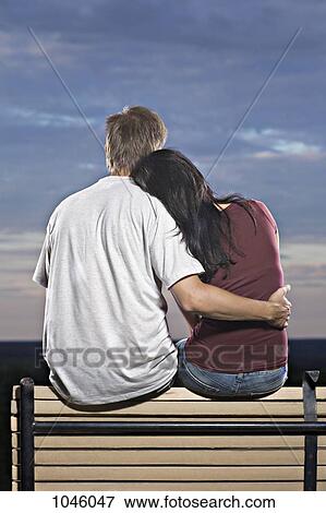 Stock Photo - A couple sitting on a bench watching the sun set. Fotosearch