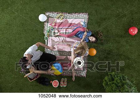 A family celebrating during a picnic in the park with cake, balloons and streamers, overhead view View Large Photo Image Stock Photo - A family celebrating during a picnic in the park with cake, balloons and streamers, overhead view. Fotosearch