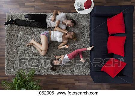 Stock Photography - A family of three happily lying on a living room rug, overhead view. Fotosearch