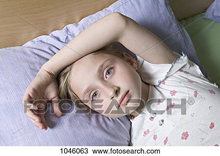 Stock Image - A girl lying on a bed, looking at camera. Fotosearch