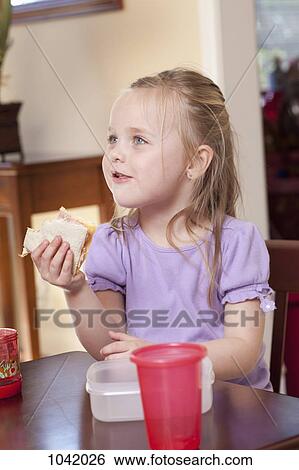 A girl sitting at a table and eating a sandwich View Large Photo Image Stock Photograph - A girl sitting at a table and eating a sandwich. Fotosearch