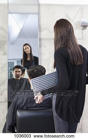 Stock Image - A hairdresser holding a mirror for a customer, rear view. Fotosearch