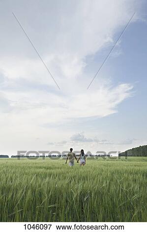 Stock Photo - A man and woman walking hand in hand through a remote field. Fotosearch
