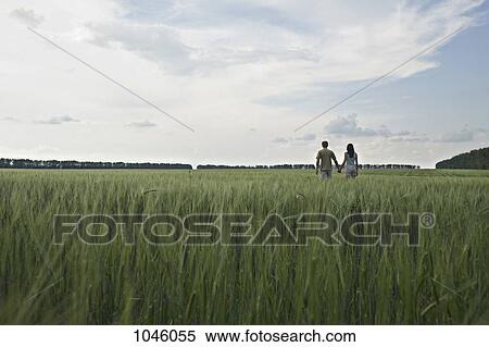 Stock Photography - A man and woman walking hand in hand through a remote wheat field. Fotosearch