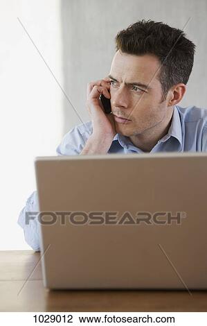 A man at a laptop on the phone View Large Photo Image Stock Image - A man at a laptop on the phone. Fotosearch