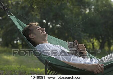 Stock Image - A man lying in a hammock petting a cat. Fotosearch