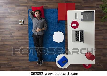 A man lying on a rug next to his home office desk, overhead view View Large Photo Image Stock Image - A man lying on a rug next to his home office desk, overhead view. Fotosearch