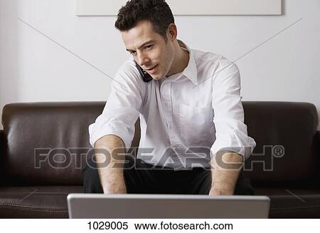 A man talking on a cordless phone while using a laptop at home View Large Photo Image Stock Photography - A man talking on a cordless phone while using a laptop at home. Fotosearch