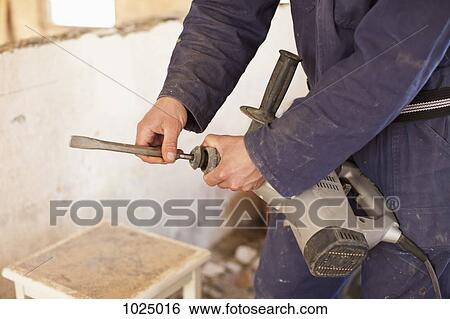 Stock Photograph - A manual worker attaching a drill bit to a drill. Fotosearch