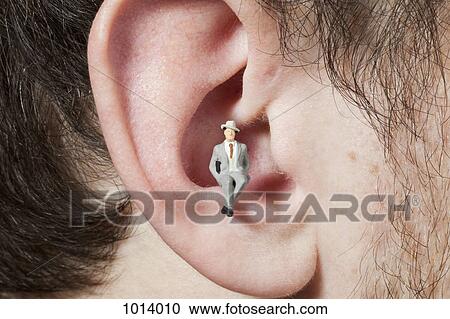 Stock Image - A miniature businessman figurine sitting in a man's ear. Fotosearch