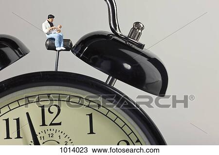 A miniature father figurine holding his baby while sitting on an alarm clock View Large Photo Image Stock Image - A miniature father figurine holding his baby while sitting on an alarm clock. Fotosearch