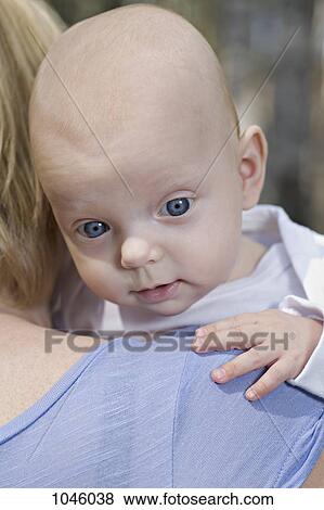 Stock Photo - A mother holding a baby, over the shoulder view, focus on baby's face. Fotosearch