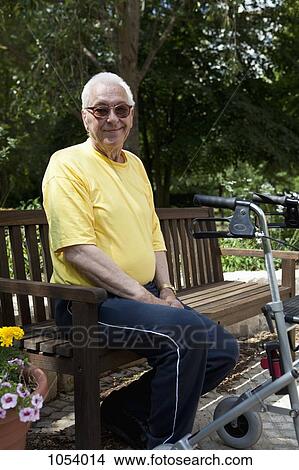 Picture - A senior man with a walker resting on a bench in the yard of his nursing home. Fotosearch