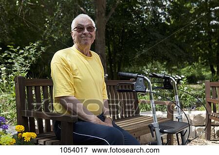 Stock Photo - A senior man with a walker resting on a bench in the yard of his nursing home. Fotosearch