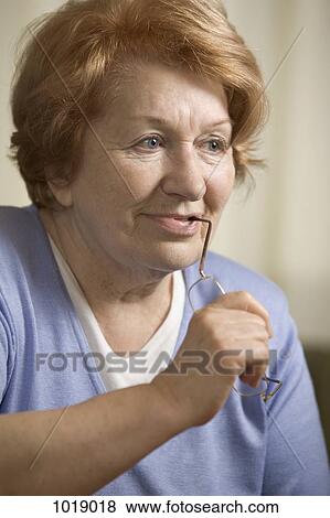 Stock Photo - A senior woman biting her glasses looking away. Fotosearch