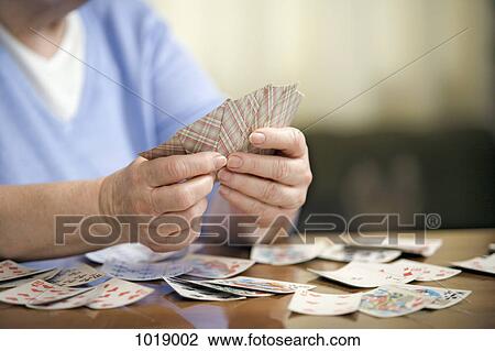 Stock Image - A senior woman playing cards, midsection, focus on hands. Fotosearch