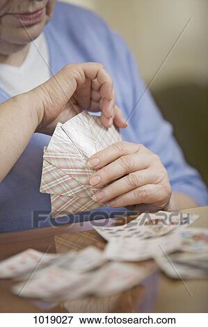 Stock Photo - A senior woman playing cards, midsection, focus on hands. Fotosearch