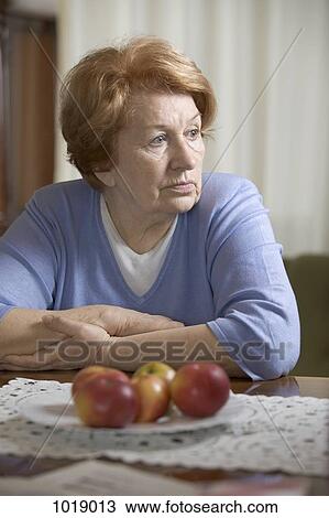 A senior woman sitting at a table looking sad View Large Photo Image Stock Image - A senior woman sitting at a table looking sad. Fotosearch