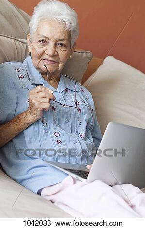 Stock Image - A senior woman sitting on a sofa with a laptop. Fotosearch