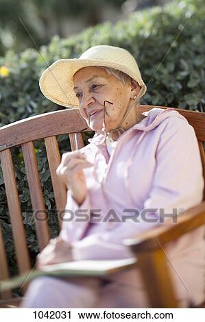 Stock Image - A senior woman sitting outside on a bench. Fotosearch