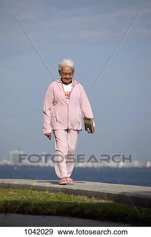 A senior woman walking on a path by the sea with a book View Large Photo Image Stock Photo - A senior woman walking on a path by the sea with a book. Fotosearch