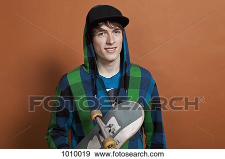 Stock Photo - A teenage boy holding a skateboard, portrait, studio shot. Fotosearch