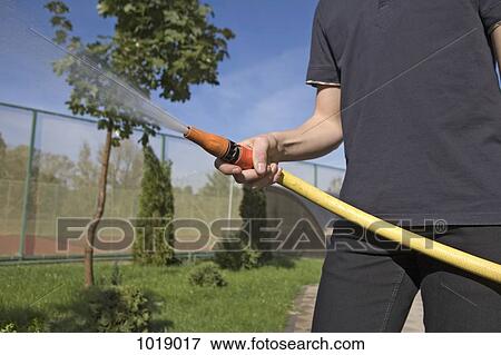 A teenage boy spraying a garden hose in a backyard, focus on hand View Large Photo Image Stock Photo - A teenage boy spraying a garden hose in a backyard, focus on hand. Fotosearch