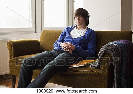 Stock Image - A teenage boy wearing headphones sitting on a couch. Fotosearch